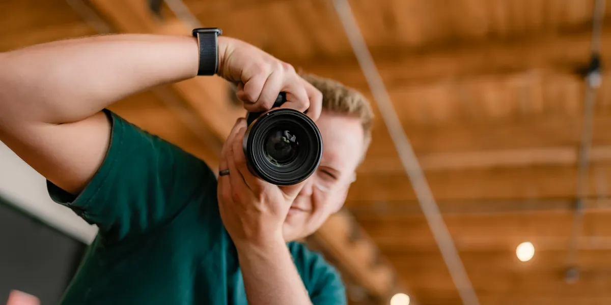 Troy framing a shot with a camera held to his eye under warm wooden beams