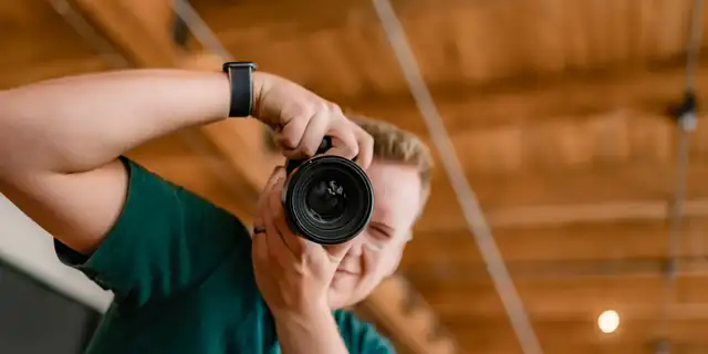 Troy framing a shot with a camera held to his eye under warm wooden beams
