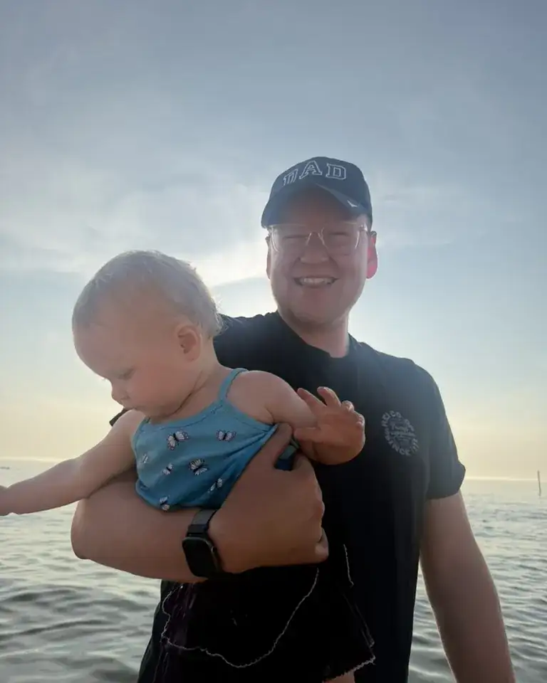 Troy holding his kid on the Lake Michigan shoreline at sunset