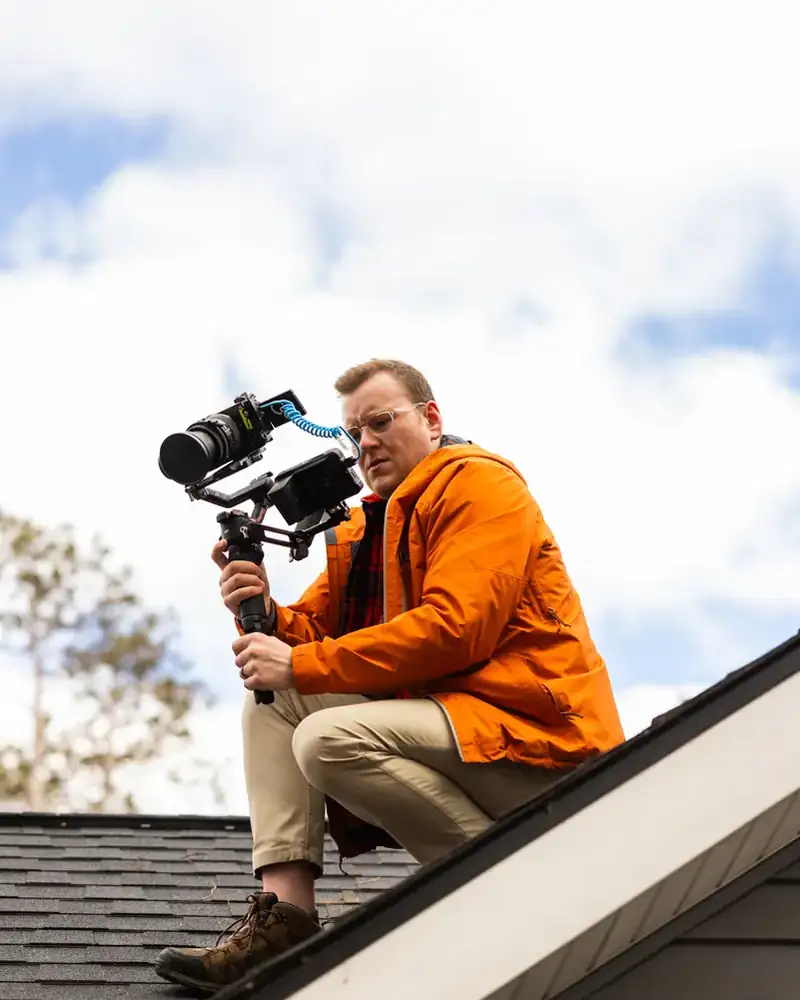 Troy on a rooftop peak with a camera gimbal, shooting against a bright sky
