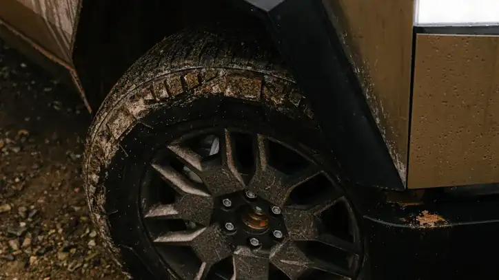 Close-up of a Cybertruck all-terrain tire and stainless fender on a gravel trail