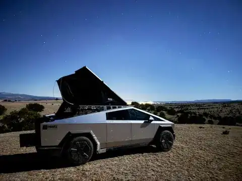 Cybertruck with a rooftop tent pitched at a campsite under a night sky