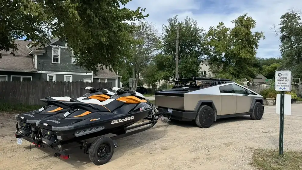 Cybertruck towing two Sea-Doos on a trailer at a lake access lot