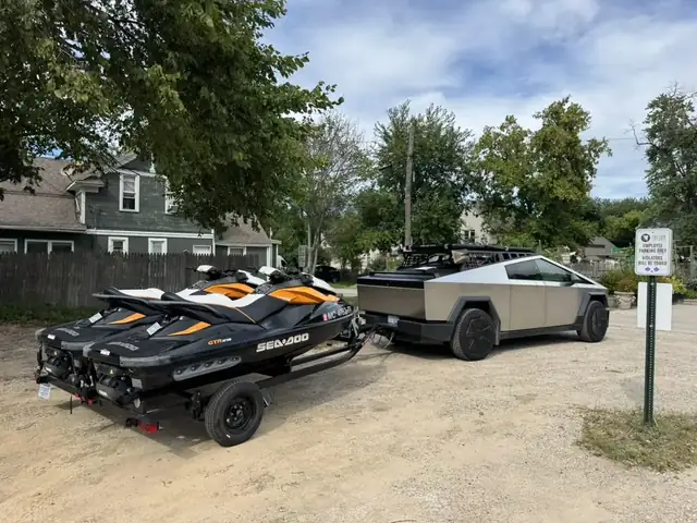 Cybertruck towing two Sea-Doos on a trailer at a lake access lot